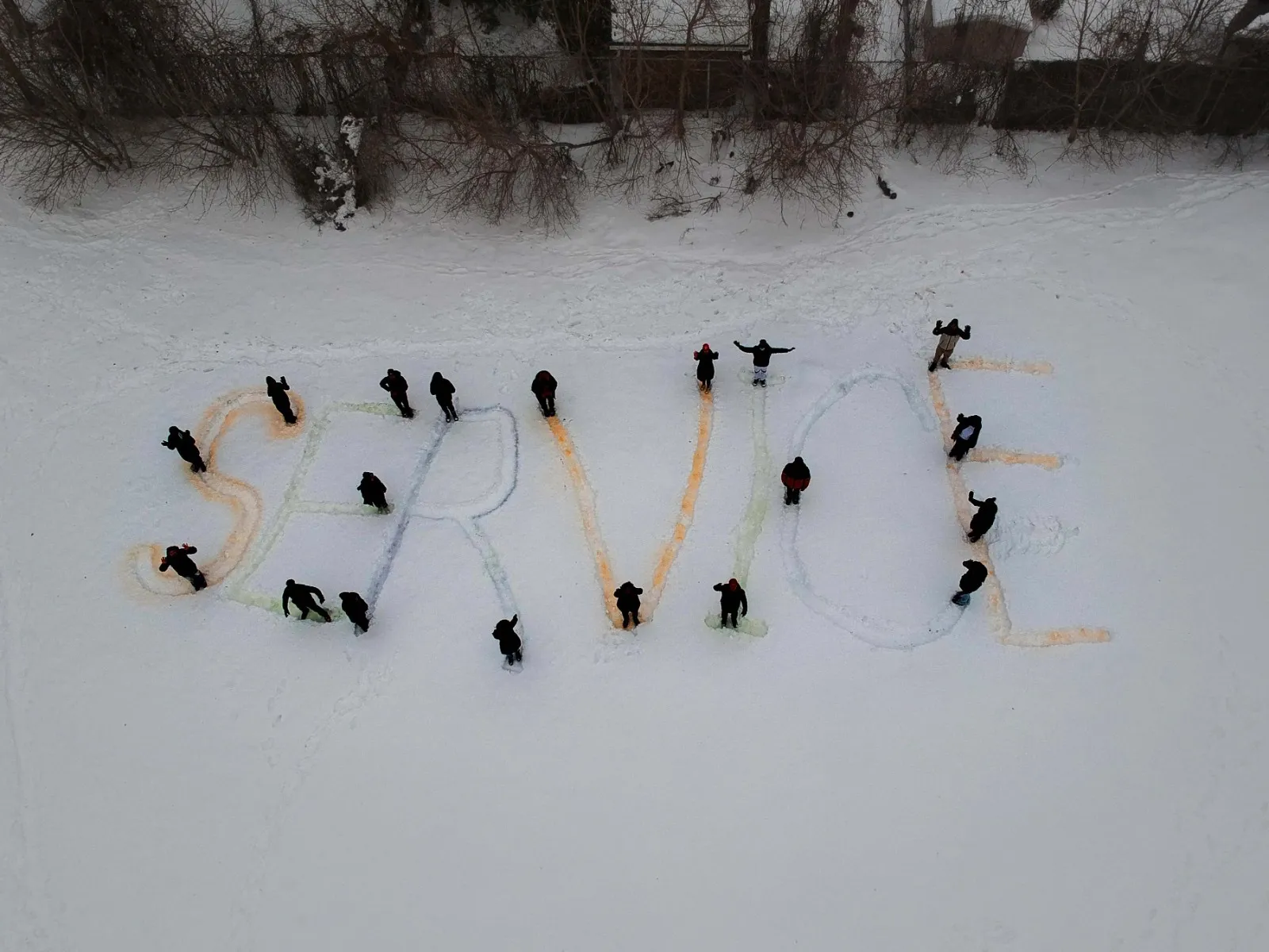 Youth spelling out the word SERVICE in the snow, viewed from above