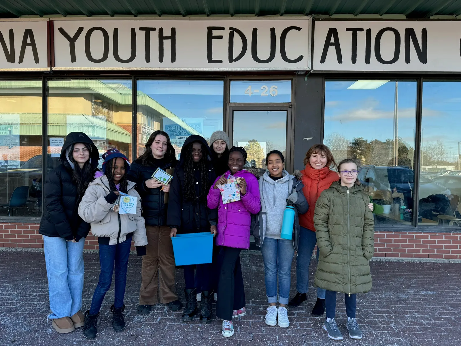 A group of youth outside a youth education centre, holding materials from a service project